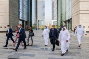 A group of Israeli entrepreneurs, including men in traditional Middle Eastern attire and suits, walk through Dubai’s urban landscape of modern high-rises. They wear face masks and carry briefcases, creating a vibrant business atmosphere.