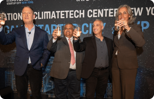 Erel N. Margalit alongside three other people stand together holding drinks in front of a backdrop that reads Climatetech Center New York. They are dressed in formal attire and appear to be celebrating or making a toast.