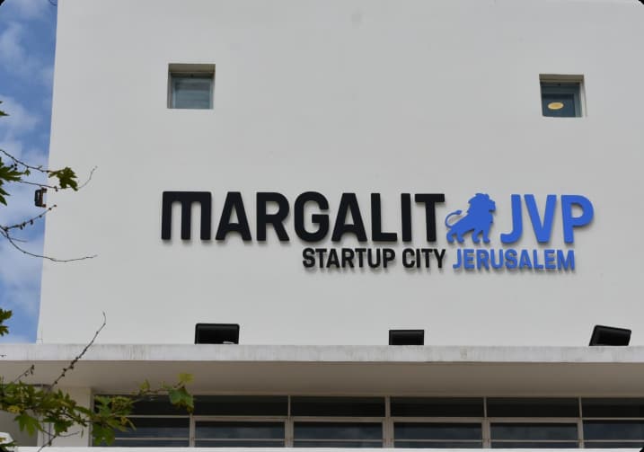 A sign on a white building displays "MARGALIT JVP STARTUP CITY JERUSALEM," featuring a blue lion logo.
