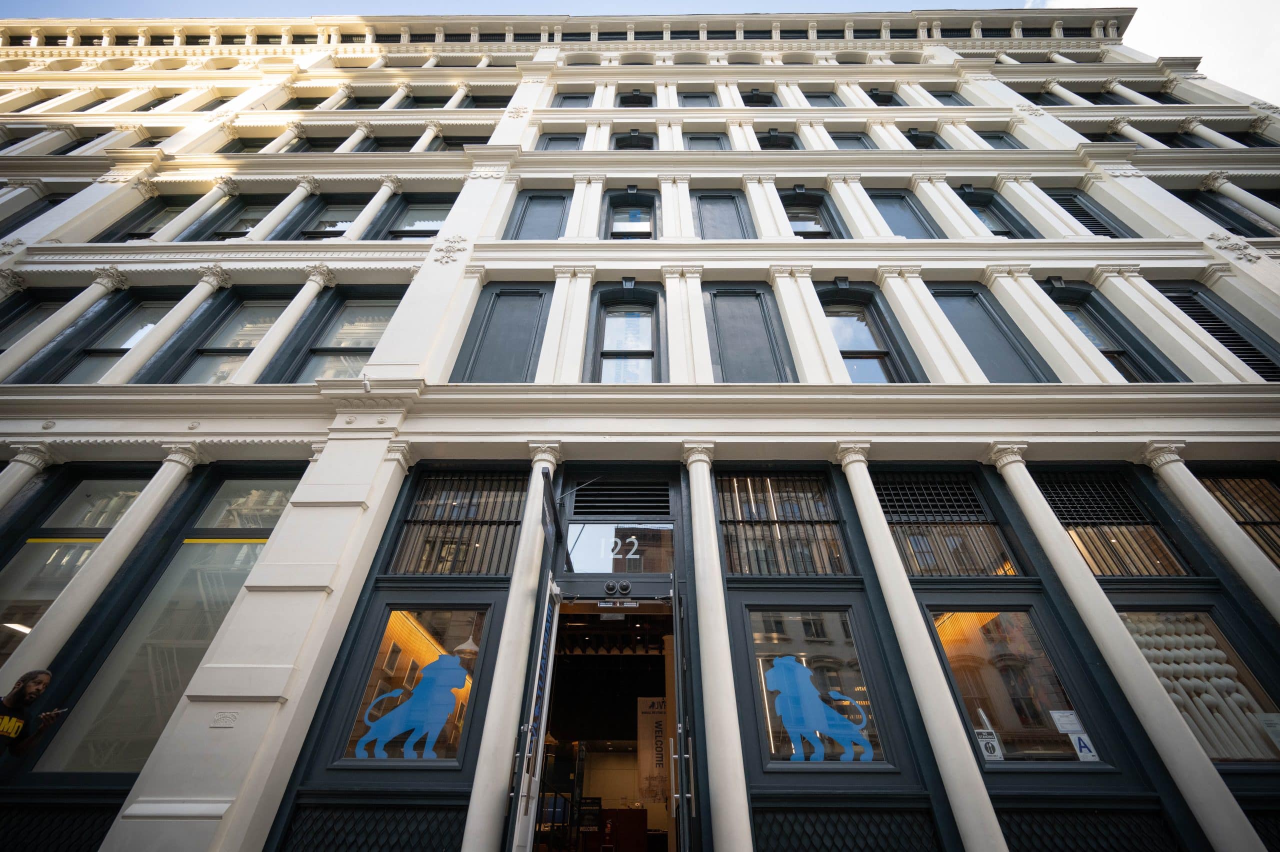 Tall, multi-story building with large windows and ornate architectural details, viewed from ground level. Two blue lion silhouettes are displayed on glass doors at the entrance.