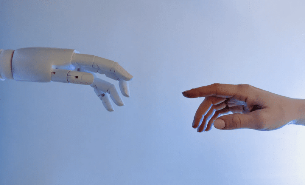 A robotic hand and a human hand reach toward each other against a light blue background, their fingers nearly touching, symbolizing the connection between technology and humanity in addressing model bias within insurance data.