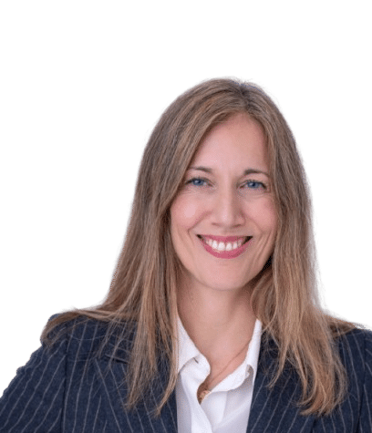 Angela Gamba, a woman with long, straight, light brown hair, smiles at the camera. She is wearing a white blouse and a dark pinstripe blazer with gold buttons. The background is transparent.