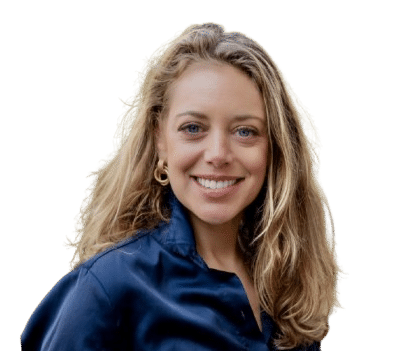Jacqueline Bouscher, with long blonde hair, wearing a dark blue satin blouse and gold hoop earrings, smiles at the camera against a plain white background.